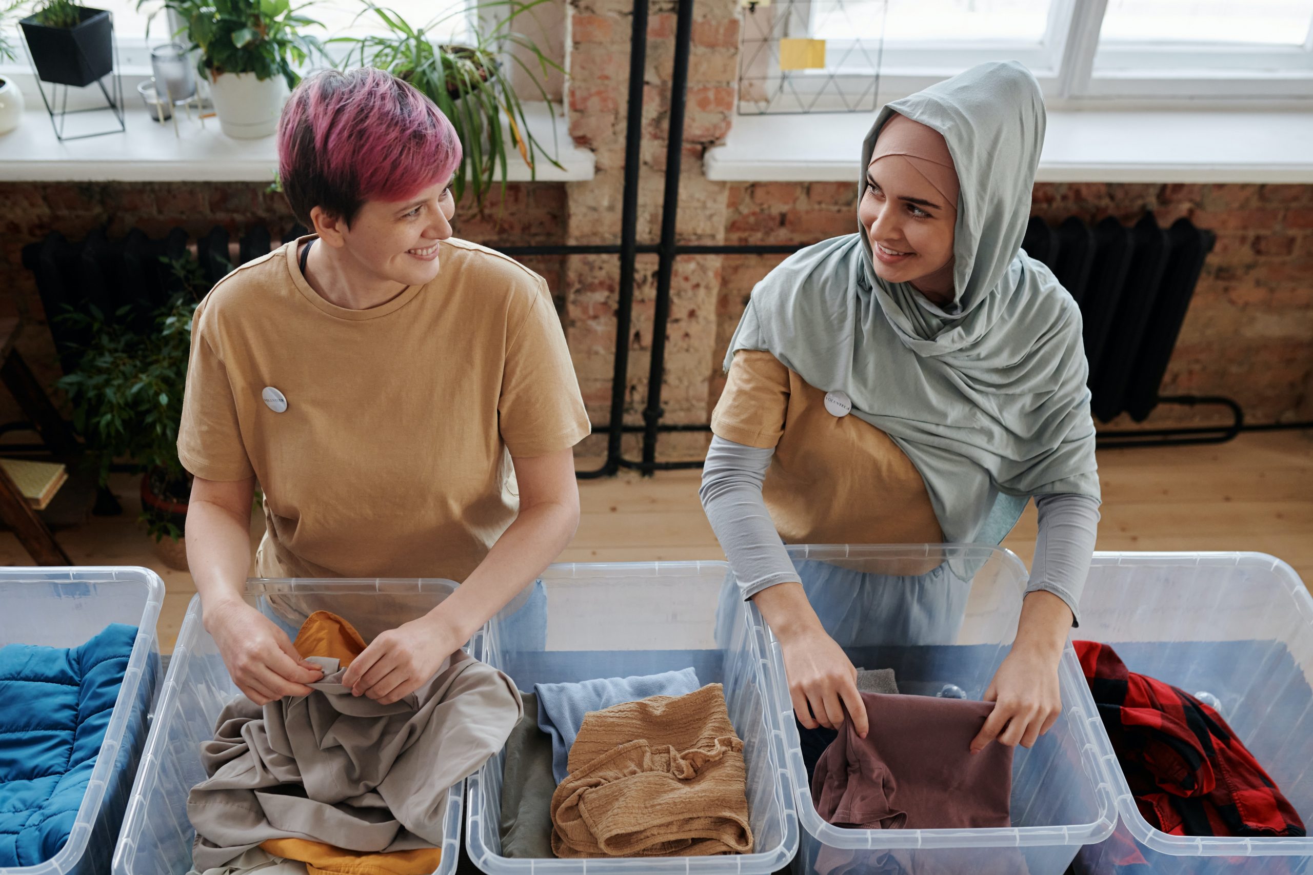 Two women standing side by side folding clothes into plastic containers